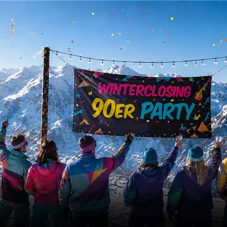 A group of people is celebrating a 90s party in the snow. In the background, impressive mountains and festive decorations can be seen.