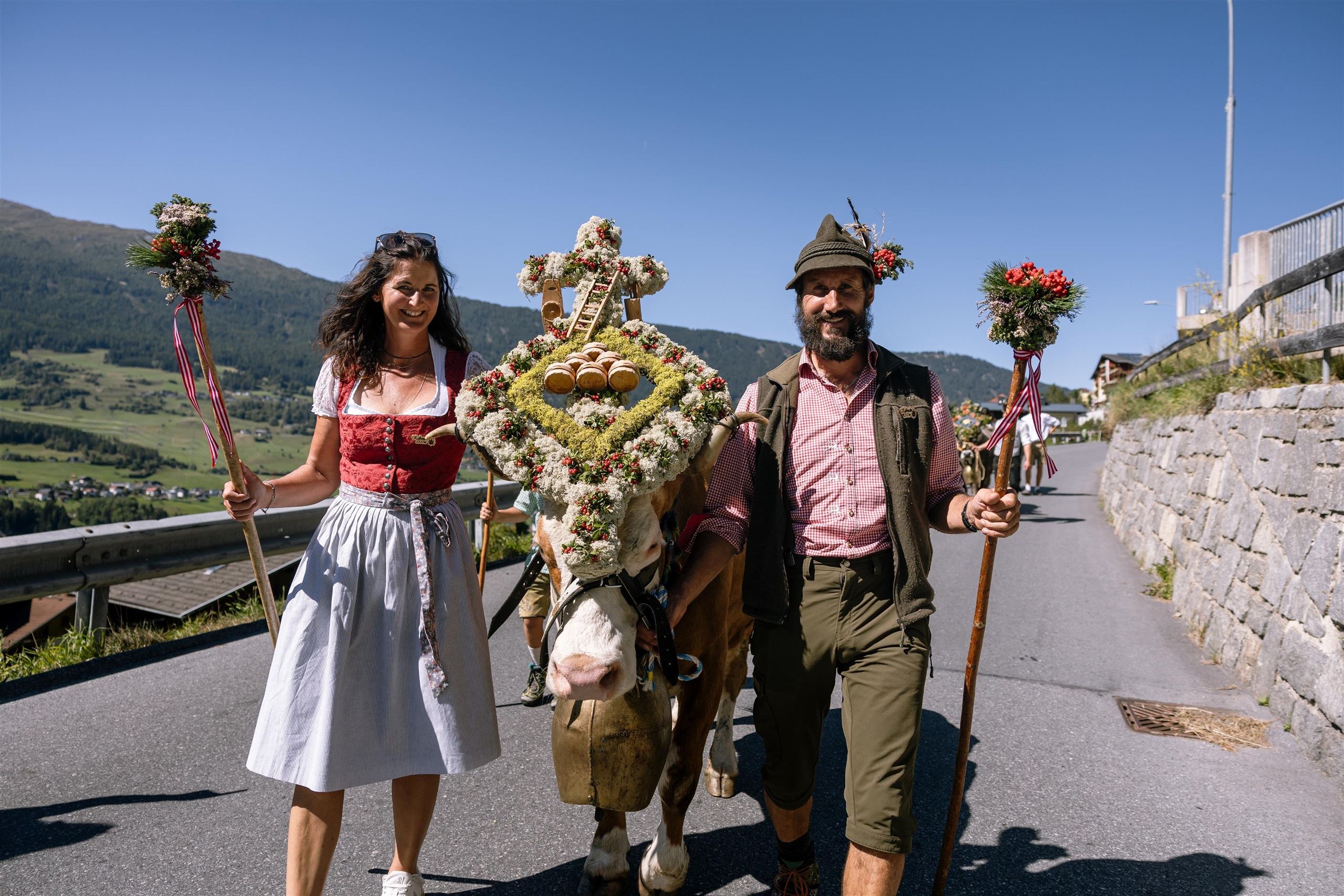Ein traditionelles Fest mit einem festlich geschmückten Pferd und zwei Menschen in Trachten. Die Umgebung ist ländlich und die Atmosphäre ist festlich und fröhlich.