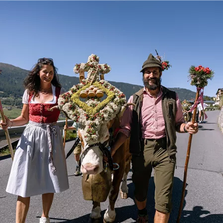 Ein traditionelles Fest mit einem festlich geschmückten Pferd und zwei Menschen in Trachten. Die Umgebung ist ländlich und die Atmosphäre ist festlich und fröhlich.