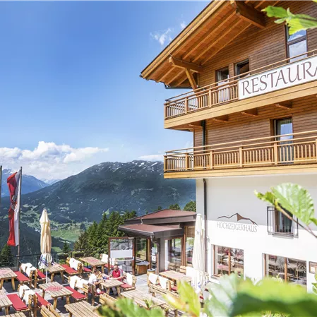 Ein gemütliches Restaurant in den Bergen mit Terrassenplätzen und Blick auf die Natur. Klare blaue Himmel und grüne Umgebung schaffen eine einladende Atmosphäre.