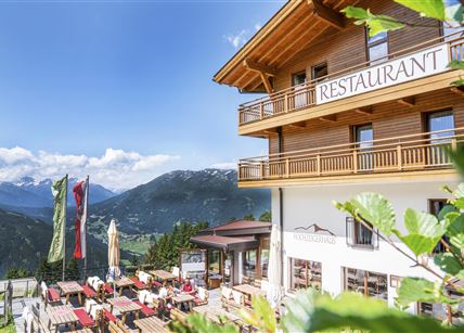 Ein gemütliches Restaurant in den Bergen mit Terrassenplätzen und Blick auf die Natur. Klare blaue Himmel und grüne Umgebung schaffen eine einladende Atmosphäre.