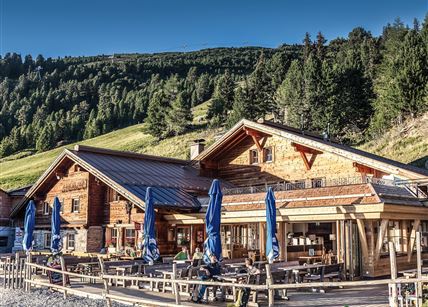 Ein malerisches Berghaus mit Holzfassade und Terrasse. Umgeben von grünen Wäldern und einer klaren Himmel.
