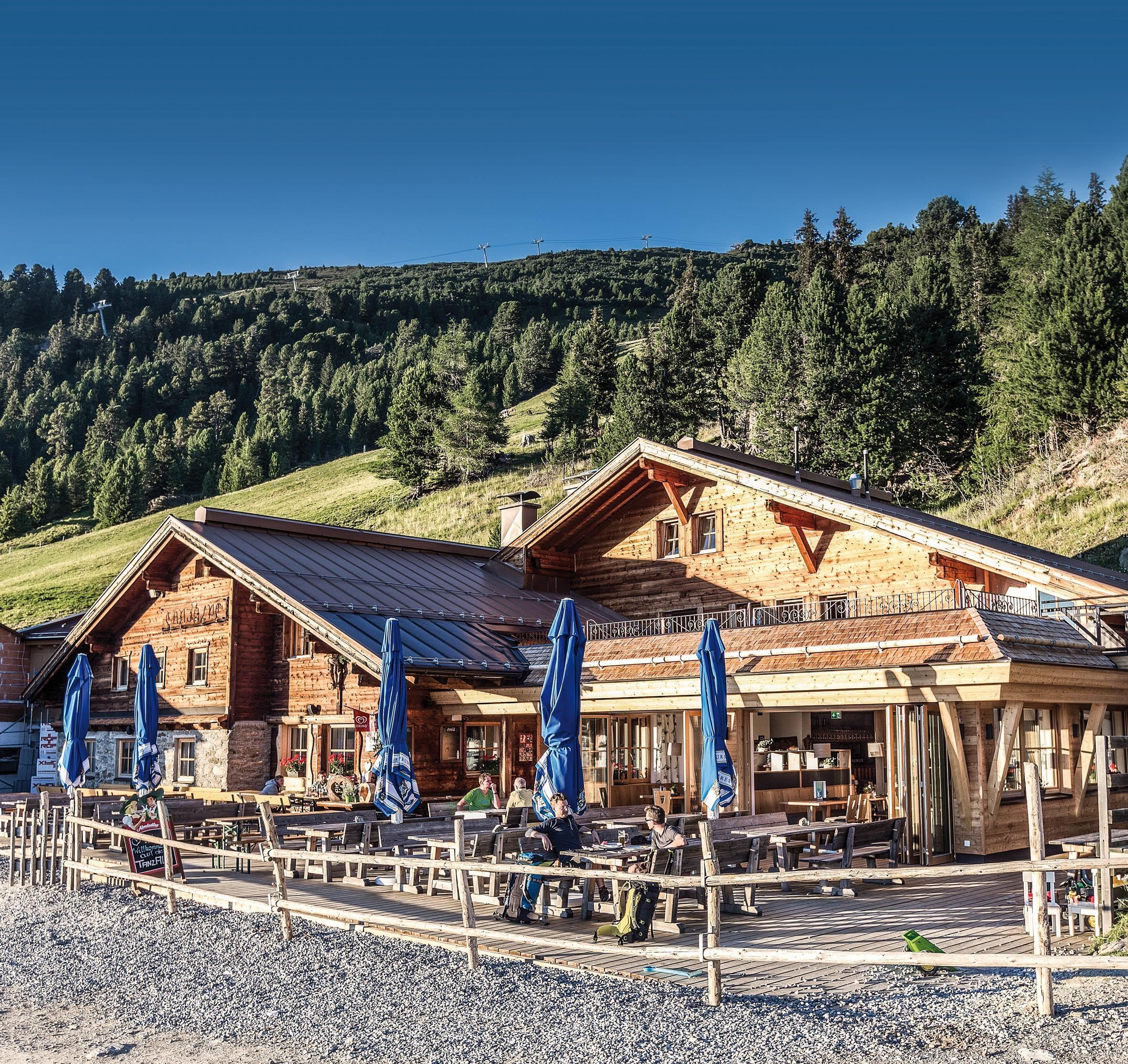 Ein malerisches Berghaus mit Holzfassade und Terrasse. Umgeben von grünen Wäldern und einer klaren Himmel.