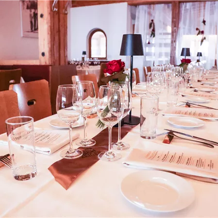 An elegantly set dining table in a restaurant with glasses, plates, and cutlery. Decorative roses and candles create a festive atmosphere.