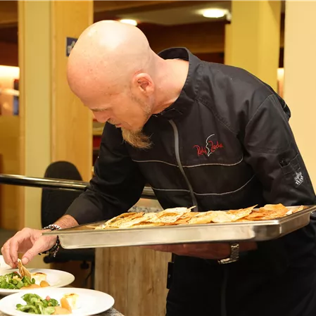 A chef carefully prepares plates with dishes. He holds a tray of food in his hand and focuses on the presentation.