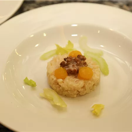 An artistically arranged plate with rice, decorated with mirabelles and a small piece of meat. Some leaves of lettuce complement the dish.